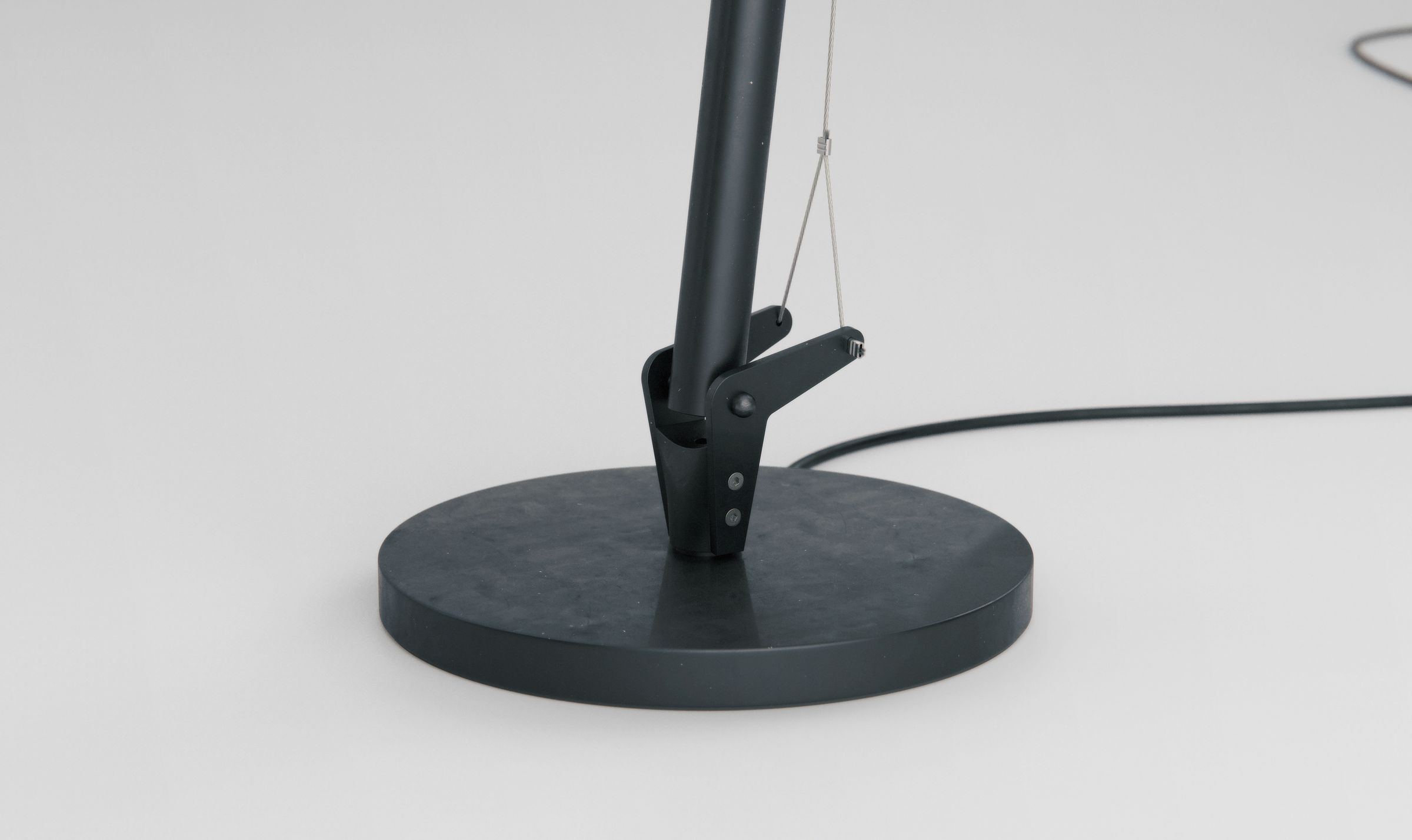 Close-up of the lamp's weighted round base and the cable routing near the bottom joint.