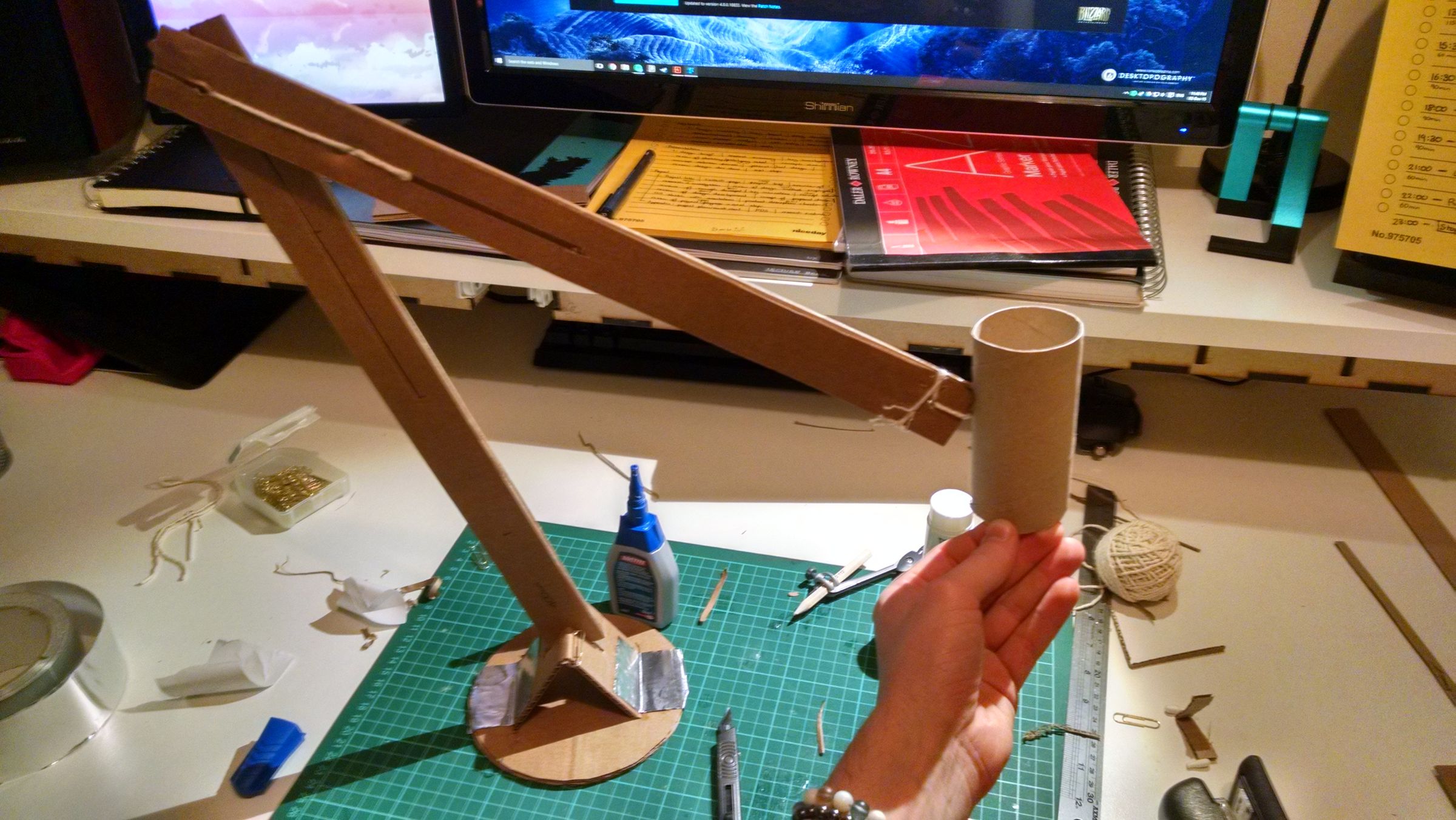 A wooden and foam mockup of an articulated desk lamp arm resting on a workbench, used to test the arm's proportions and range of motion.
