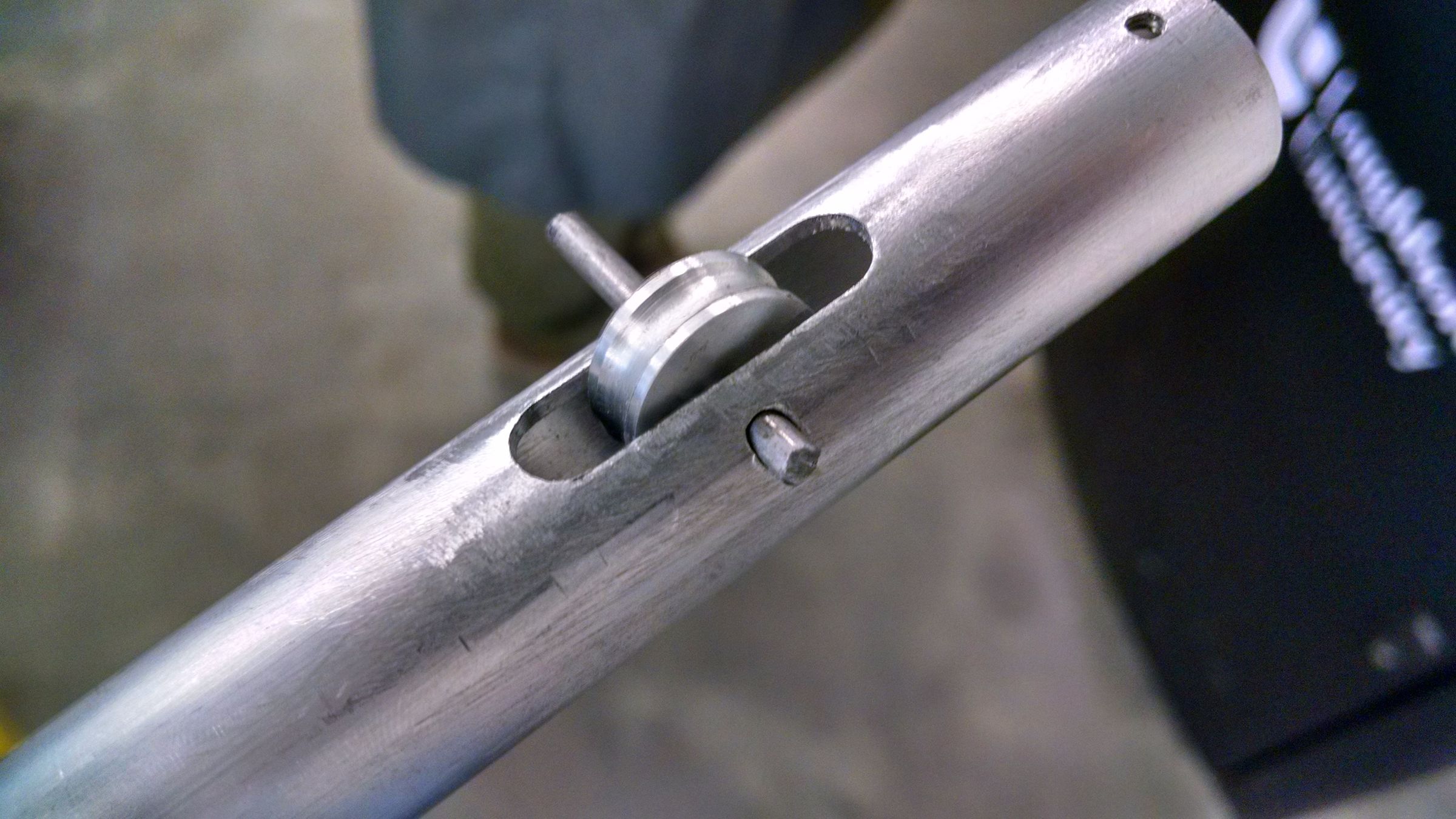 Close-up of a hand holding a machined metal tube with a slot cut into it, part of the lamp's arm assembly.