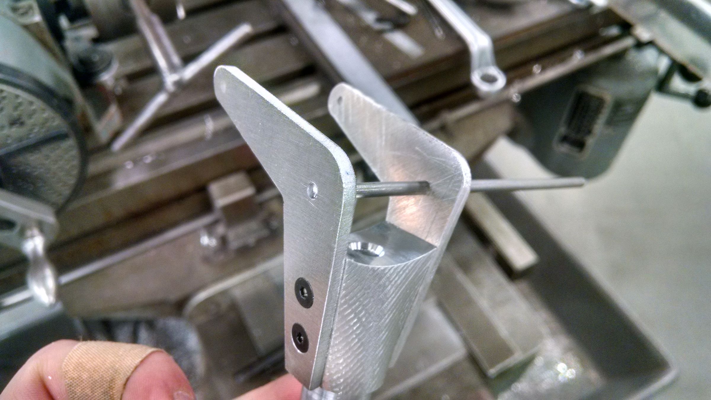 Close-up of hands assembling a metal hinge bracket on a workbench.