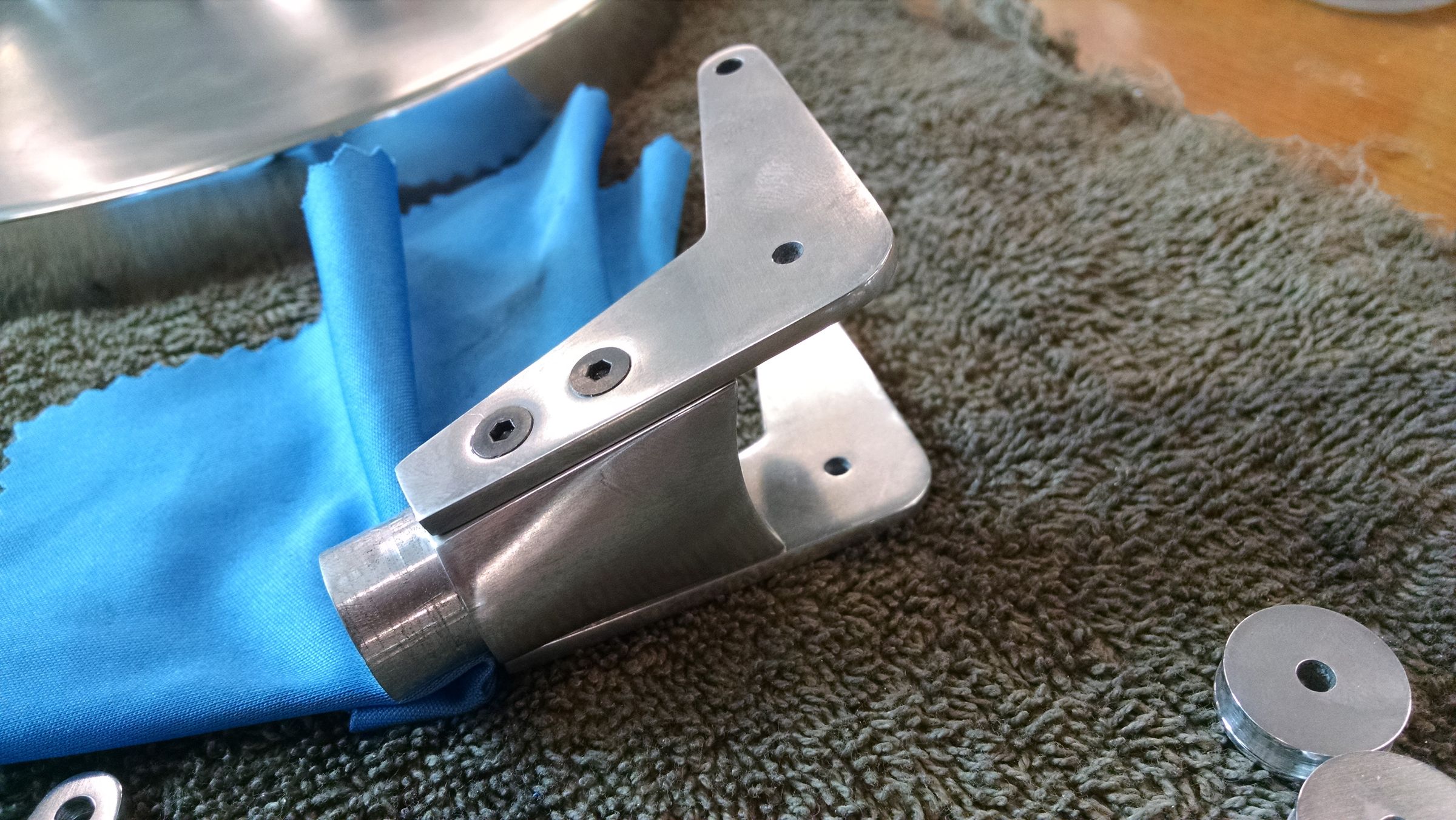 A hand holding a metal hinge bracket assembly, partly wrapped in blue protective tape, on a workbench.