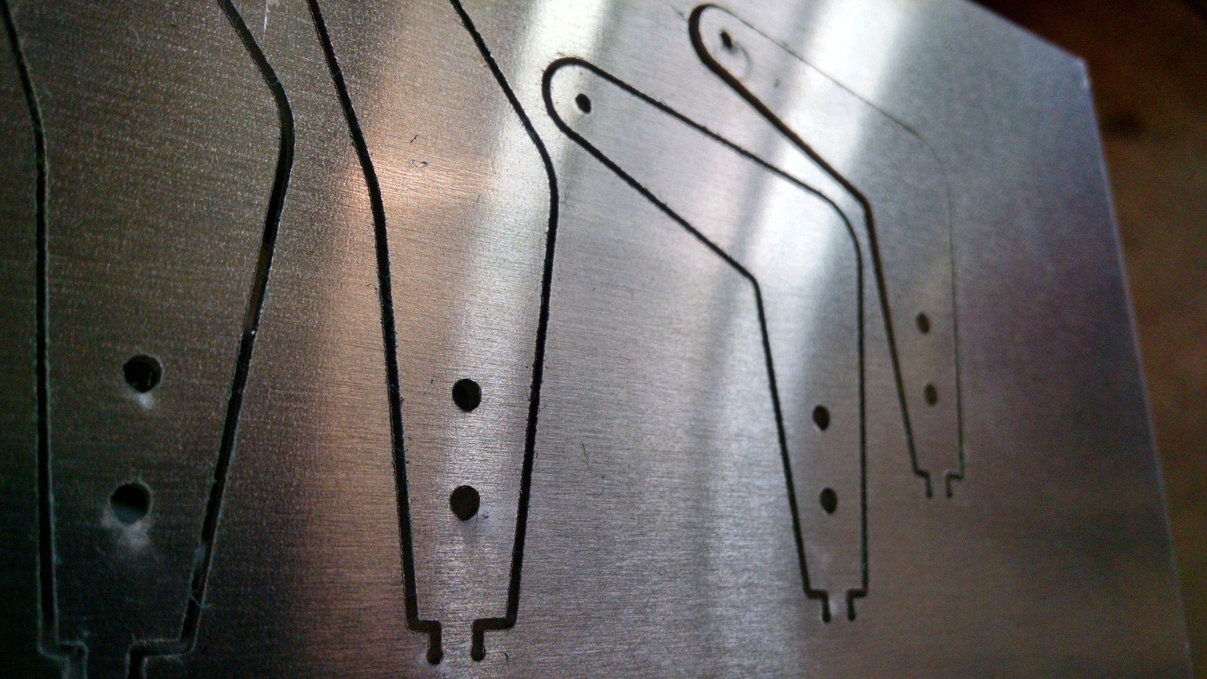 Close-up of flat, laser-cut metal hinge brackets with drilled holes, laid out on a workbench.