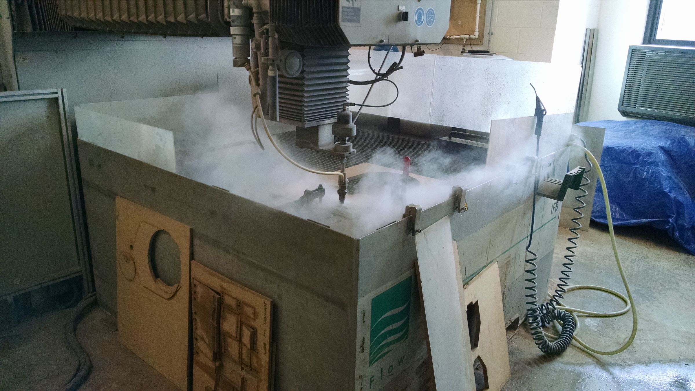A CNC machine cutting a metal component, with coolant mist rising from the cutting area.