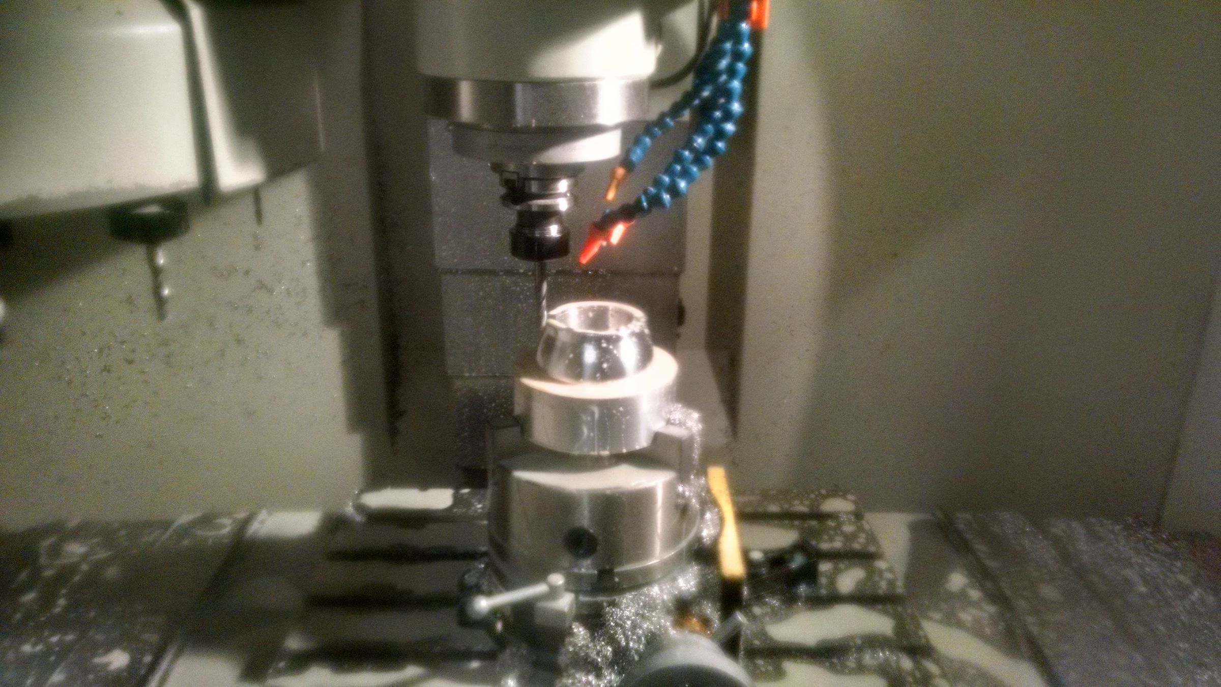 Close-up of a lathe turning a cylindrical metal part, chuck jaws visible gripping the workpiece.