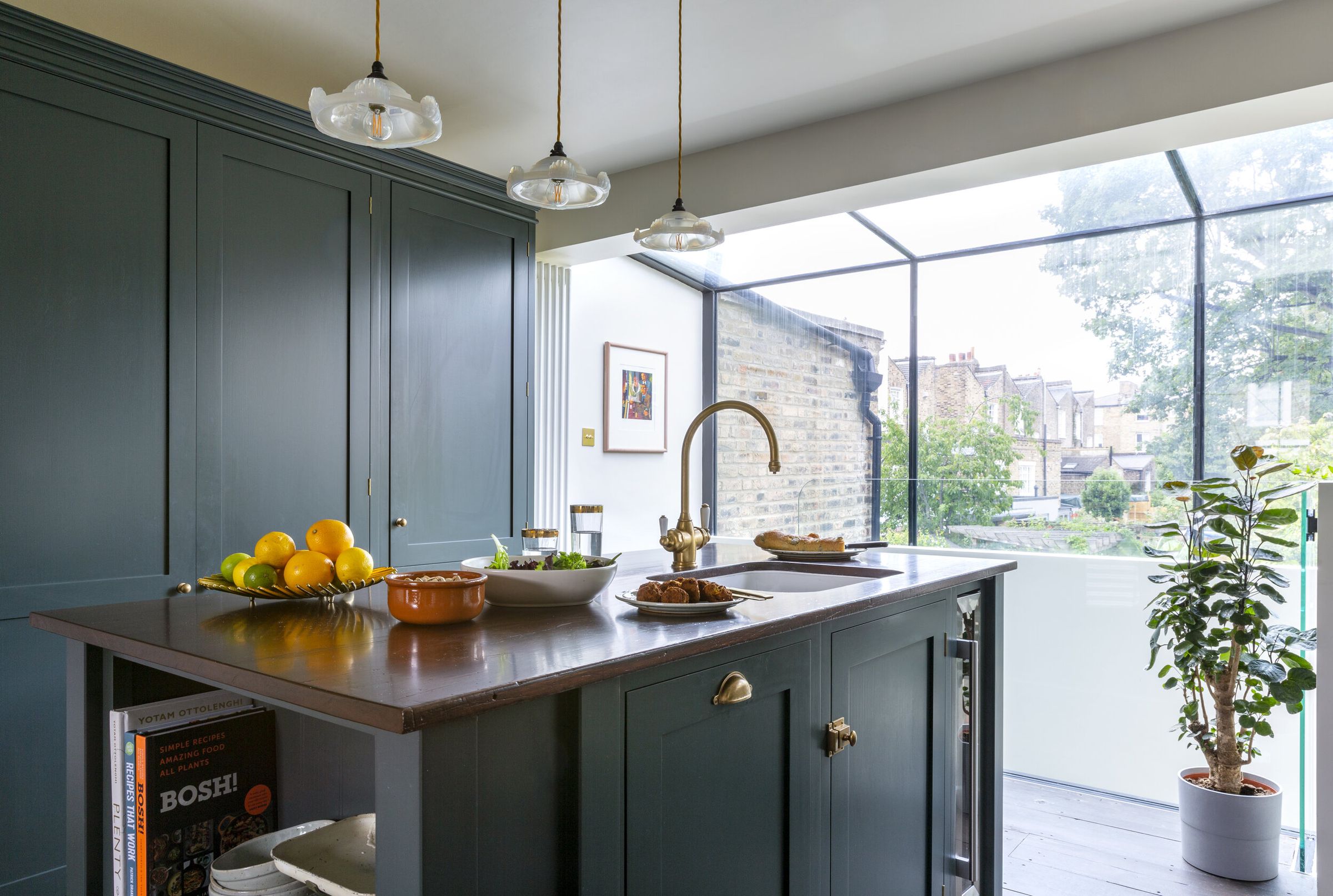 Wide view of the kitchen island with a wooden countertop and brass tap, under a glazed conservatory-style roof.