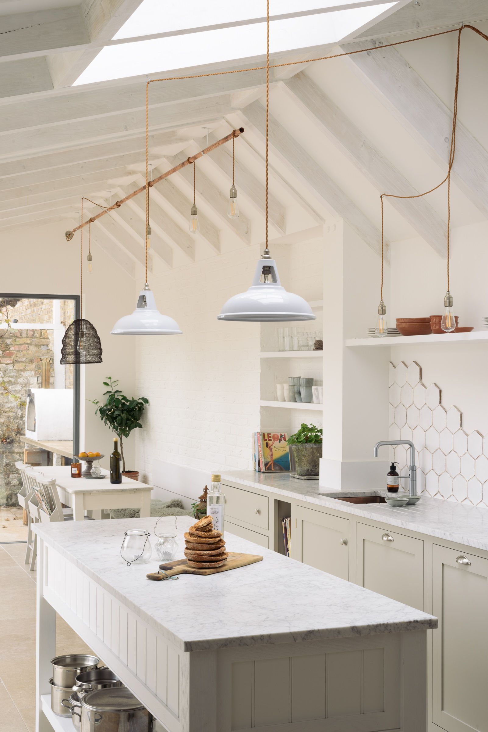 Wide view of the vaulted kitchen extension, showing exposed white roof beams, pendant lights, and a marble-topped island.