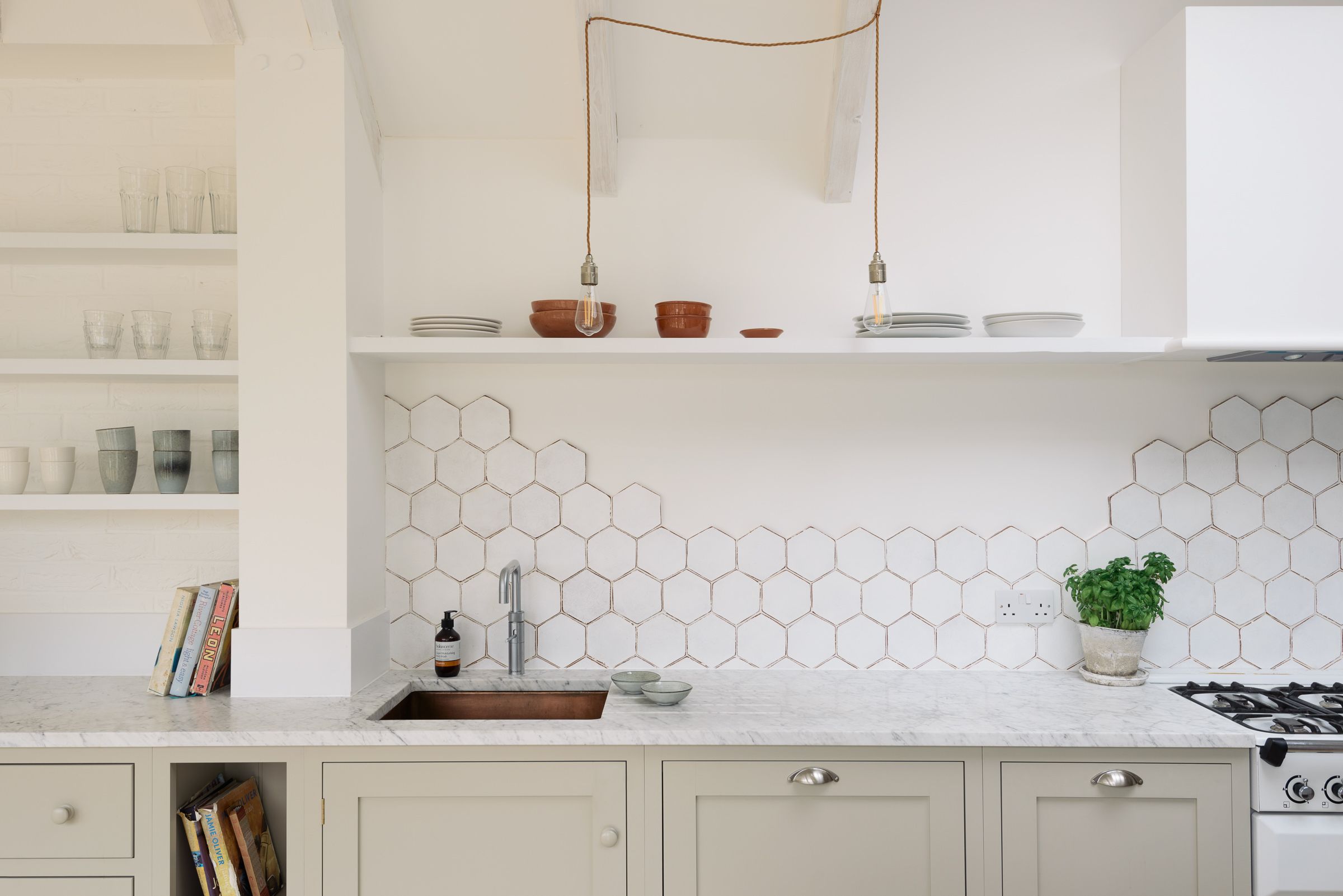 Close-up of a hexagonal tiled splashback, open shelving, and pale green cabinetry around the sink.