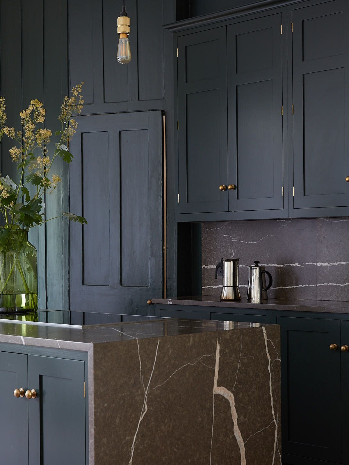 Close-up of a dark marble countertop and matching splashback with bold veining, flanked by brass cabinet handles.