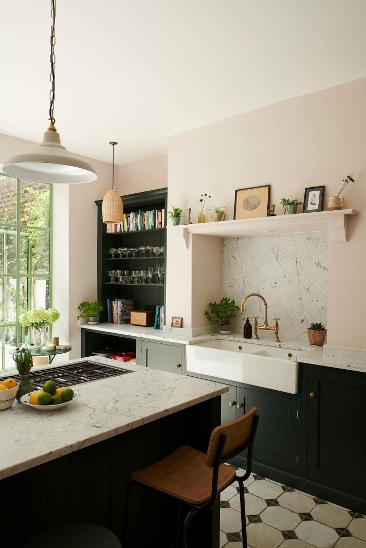 Wide view of the kitchen showing the marble-topped counter, dark green cabinetry, open shelving, and a breakfast bar stool.
