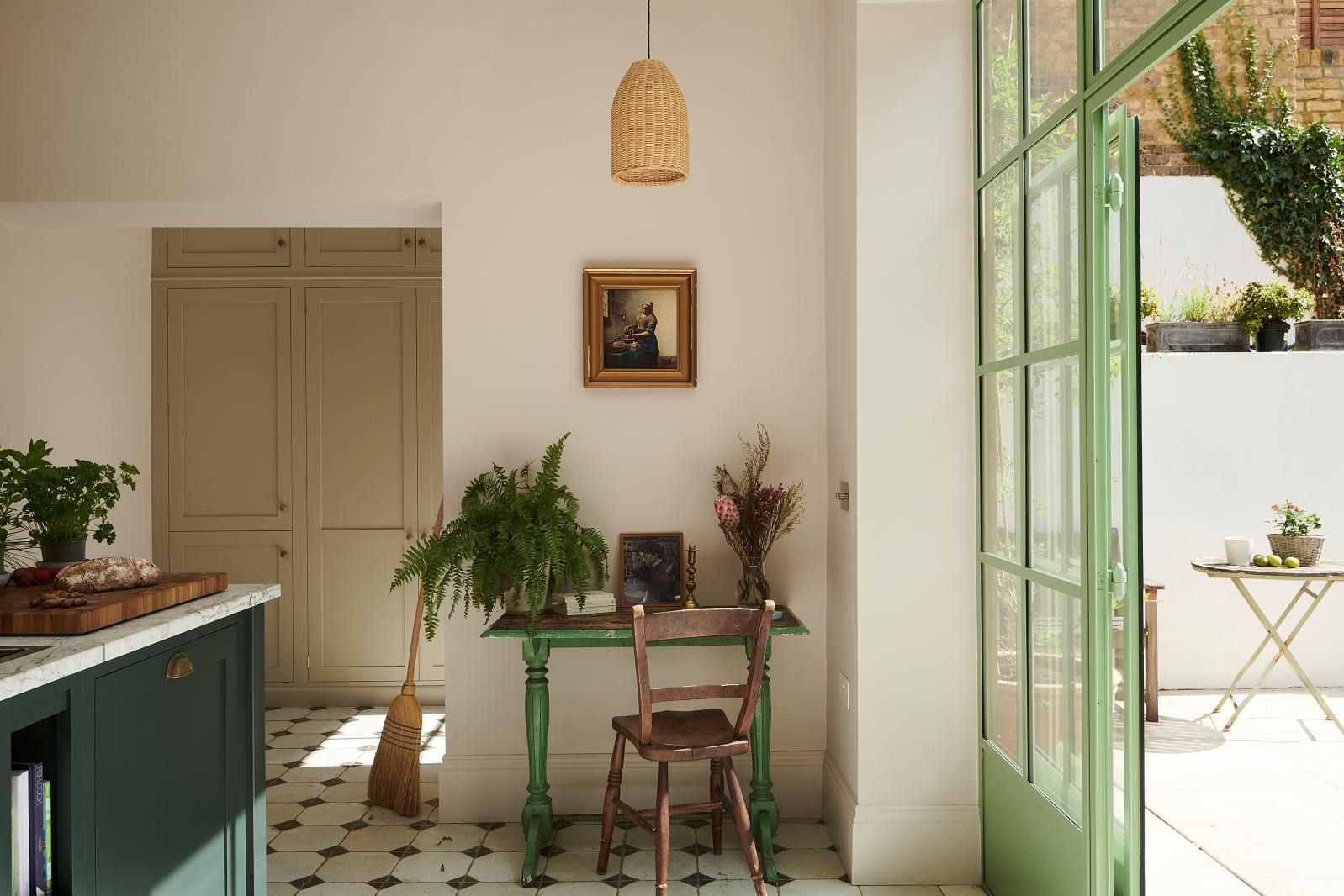 View across the kitchen toward a hallway with a green console table and glazed doors opening onto a courtyard.