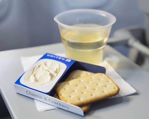 Photo of a cracker and cheese snack package on an airline table with a glass of wine in the background.